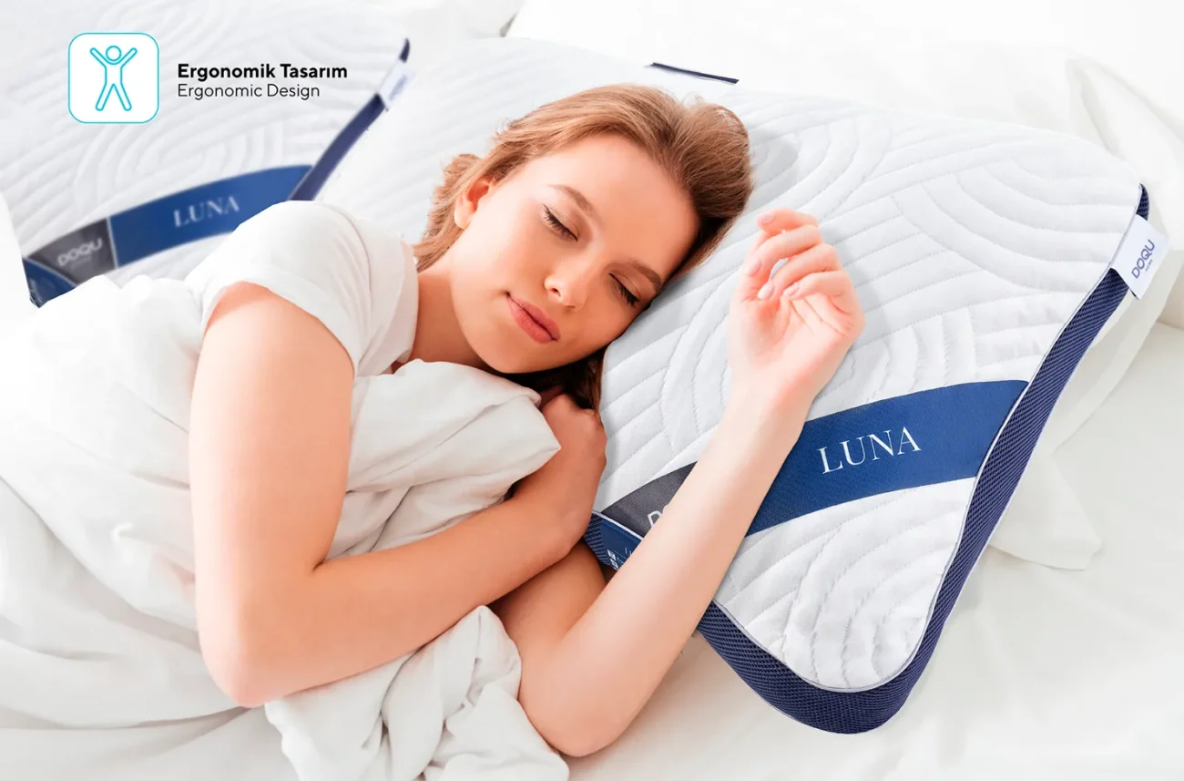 O femeie tânără și fericită care doarme liniștită pe perna anatomică și moale Luna în patul ei confortabil